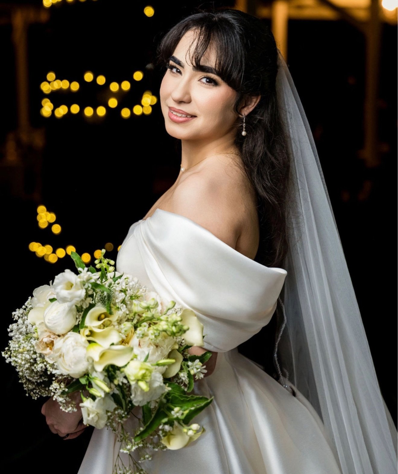 Novia sosteniendo un ramo de rosas blancas con velo largo de satín.