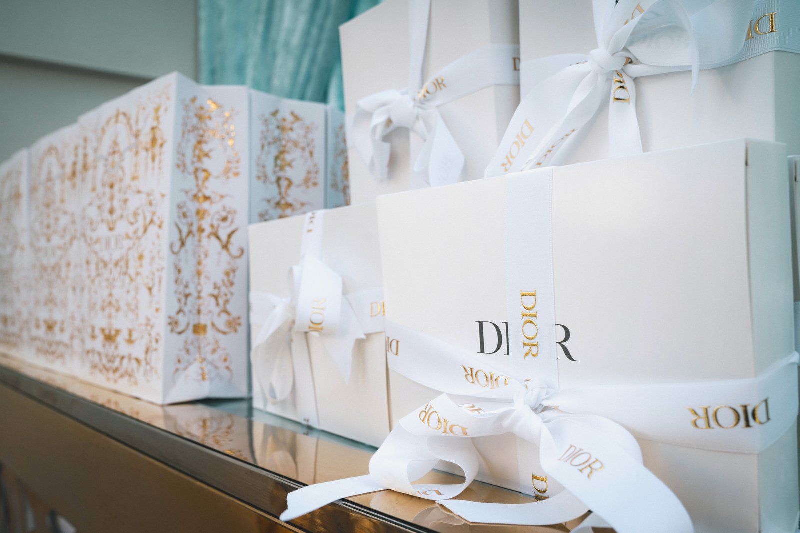 Cajas y bolsas de regalo Dior con acabado dorado y moños blancos.