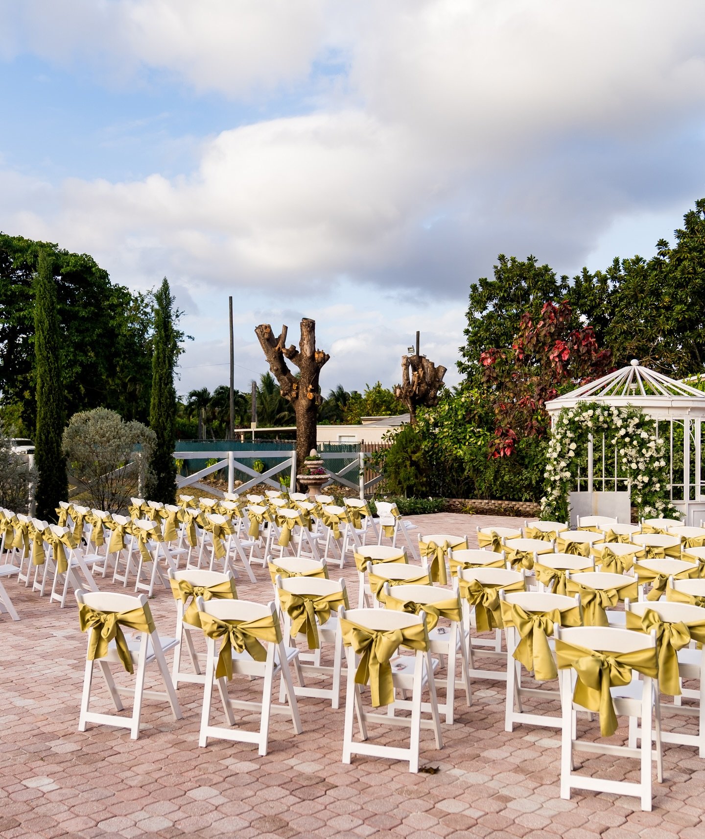 Ceremonia de boda al aire libre con sillas blancas y moños dorados.