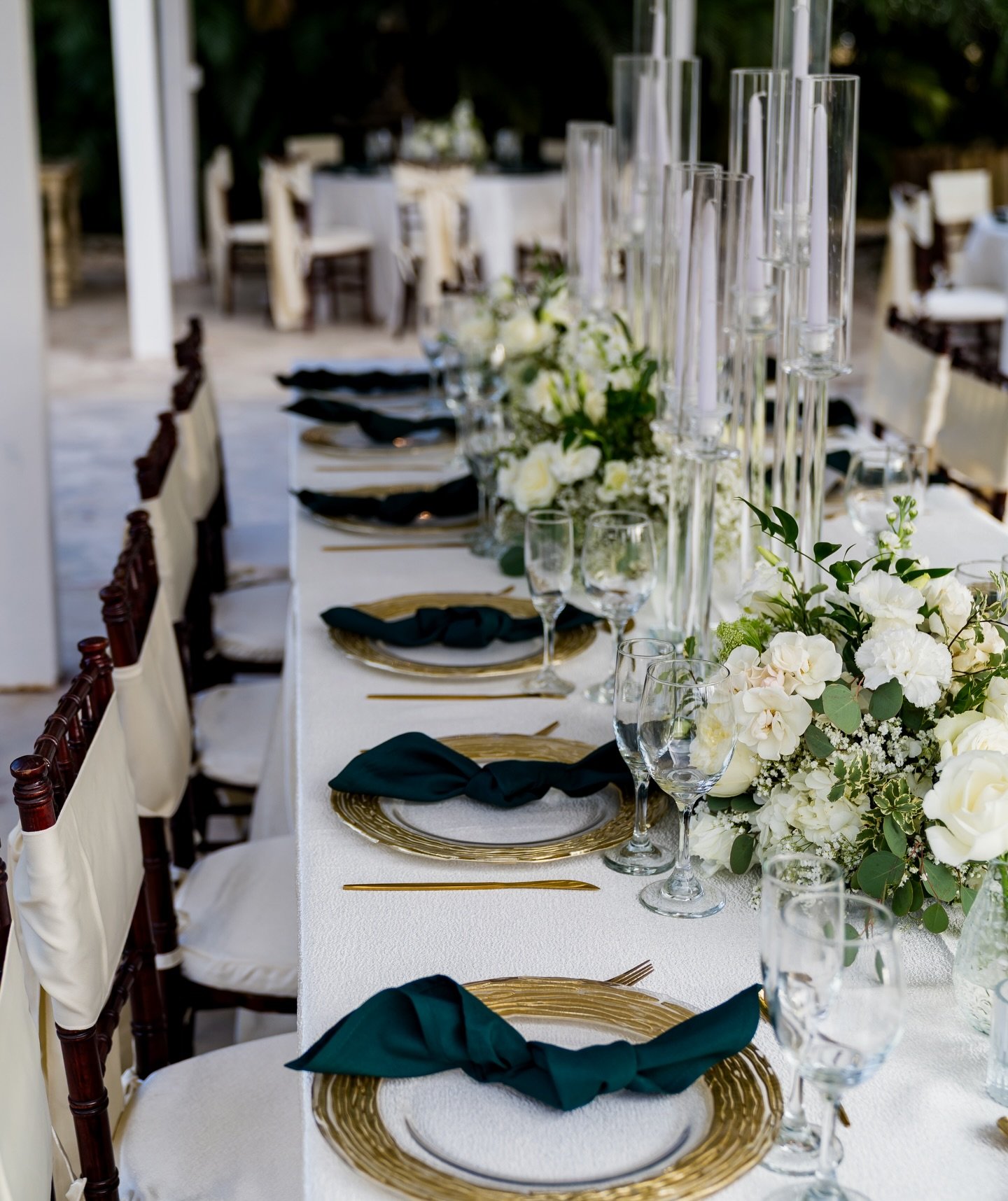 Mesa de recepción nupcial con mantel blanco, servilletas verde esmeralda y cristalería.